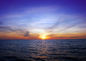 Obraz premium A golden orange sun sets with its reflection shivering over the deep blues waters of the Gulf of Mexico, with a deep blue and purple tones