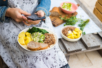 Woman take picture of food with phone at kitchen or summer cafe. Smartphone photography of vegetables dinner or lunch for blogging or social media publications. Vegan vegetarian healthy diet.