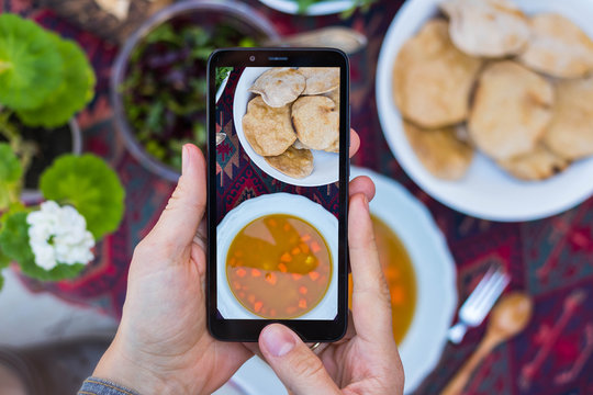 Woman take picture of food with phone at kitchen or summer cafe. Smartphone photography of vegetables dinner or lunch for blogging or social media publications. Vegan vegetarian healthy diet.
