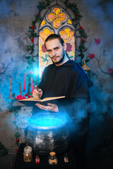 Fototapeta premium The mage is cooking a potion. A male wizard in a black mantle with a magic wand and a book. He casts a spell over the witch's cauldron. Guy in an old castle with luminous magic