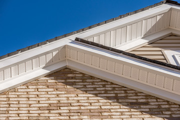 Close up view of two gables, white fascia  joining together on a house covered with brick siding
