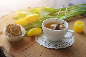 Sunny morning with cup of tea with marshmallow and yellow tulips on wooden table
