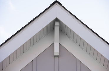 White decorative corbel, bracket, brace on a triangle gable roof, white soffit and fascia, PVC or vertical vinyl lap siding with blue sky background © tamas