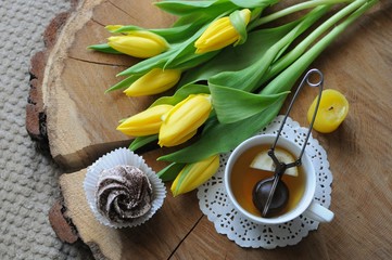 Cup of green tea with lemon on wooden table with marshmallow and yellow tulips.