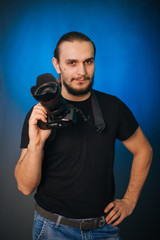 Photographer in a black T-shirt on a blue background. The guy with the camera. Photographs in the studio.