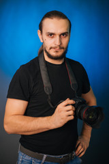 Photographer in a black T-shirt on a blue background. The guy with the camera. Photographs in the studio.