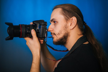 Fototapeta premium Photographer in a black T-shirt on a blue background. The guy with the camera. Photographs in the studio.