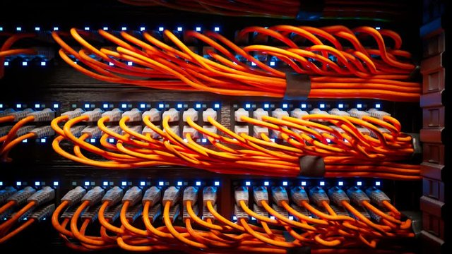 Countless orange cables in a  server cabinet lit by a single spotlight. 4KHD
