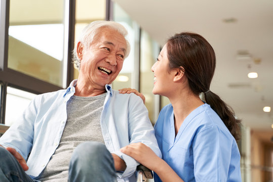 young friendly asian female caregiver talking to elderly man in nursing home