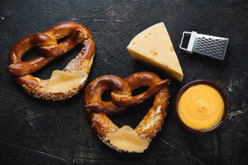Cheese dipping sauce and pretzels on a dark-brown stone background, flatlay, studio shot