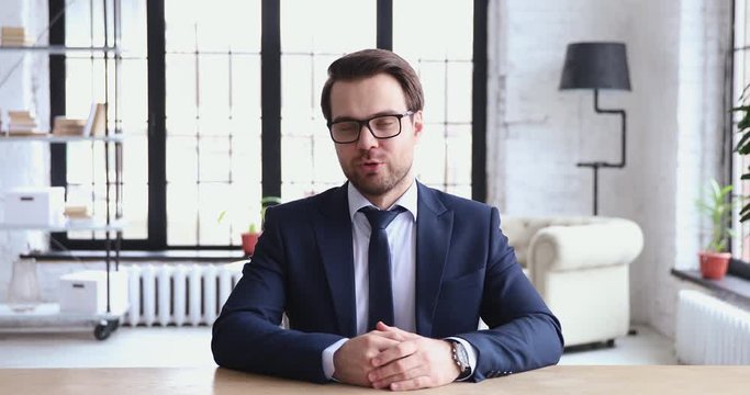 Young ceo speaking to camera recording business video presentation. Confident businessman wearing suit and tie looking talking to web cam streaming webcast training, doing conference call in office.