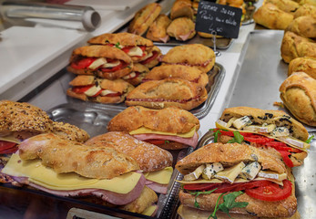 Stack of hot dogs in baguette buns covered with melted cheese on display at a local sandwich shop in Nice, France