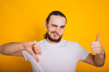 A guy with a beard in a white T-shirt on a yellow background shows a class or like. Holds thumbs up...