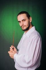 Wizard man in a white shirt conjures. A guy with long hair and a beard holds a magic wand on a...