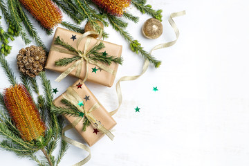 Beautifully wrapped gifts with gold ribbon and surrounded by Australian native Banksia, glitter, cream pine cones and other Christmas decorations surround them