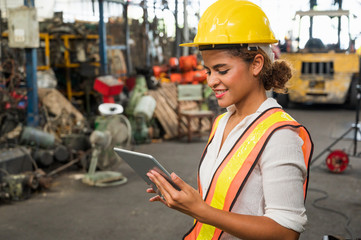 Female industrial worker working and checking machine in a large industrial factory with many equipment.