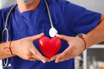 Male doctor wearing blue uniform hold in arms red toy heart closeup. Cardio therapeutist, student education, CPR, 911 life save, physician make cardiac physical, pulse rate measure, arrhythmia