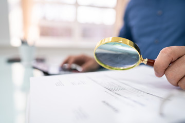 Businessperson Checking Invoice With Magnifying Glass