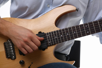 Male arms holding and playing classic shape wooden electric guitar closeup. Six stringed learning...