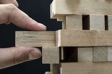 Close up of man's hand take one block to a tower of wooden blocks, dark tone.