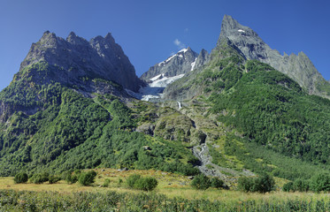 Fototapeta na wymiar Caucasus Mountains, Dombay. Rocky peaks, glacier and green forest on the slopes. Sunny summer day.