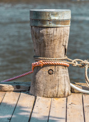 A rope is tied to a wooden mooring bollard with the Yarra River,  Melbourne, Australia in the...