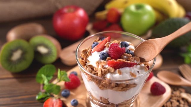 Scooping Yogurt with granola and fruits .	