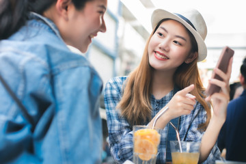 Young Asian female friends taking her vacation and eating street food  In Bangkok. asian woman relax and talking with happiness emotion.She shoot photo by mobile phone with friend.