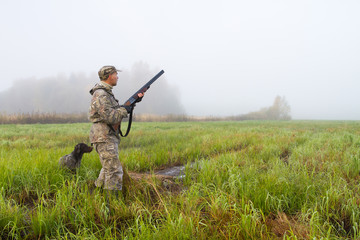 a hunter with a dog stands in a wet meadow