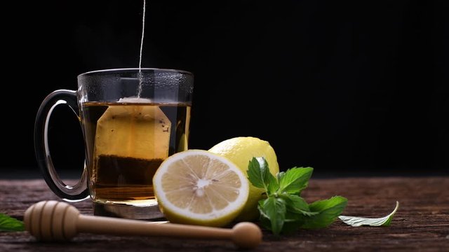 lemon tea in glass with mint and sliced lemon on wooden table and black background .