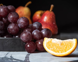 frest fruits on plate, bunch of purple grapes, ripe pear and fresh orange close-up