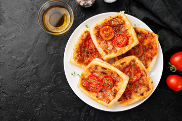 Puff pastry mini pies with cheese and tomatoes on black background