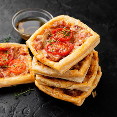 Puff pastry mini pies with cheese and tomatoes on black background