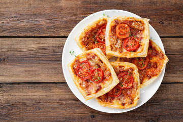 Puff pastry mini pies with cheese and tomatoes on wooden background