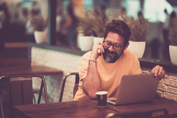 Adult man worker with laptop computer and coffee working at the bar in co work space - people in...
