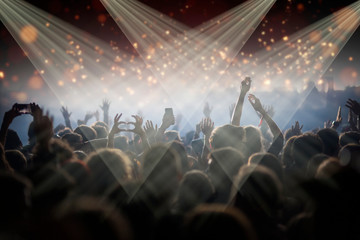 Stage lights and crowd of audience with hands raised at a music festival. Fans enjoying the party vibes.