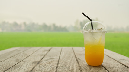 Orange juice with ice in plastic mug on a wooden table with a natural green background.