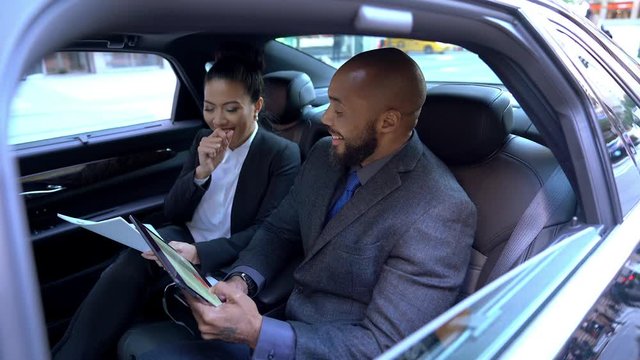 Formally dressed financial specialists working with reports during destination way in executive car, cheerful diverse male and female traders browsing website for making online money transfer