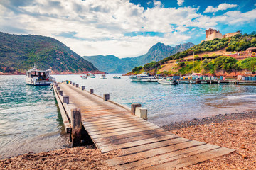 Old wooden pier in Port de Girolata - place, where you can't get by car. Sunny summer scene of Corsica island, France, Europe. Beautiful Mediterranean seascape. Traveling concept background..