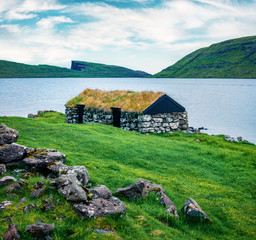 Lonely house with turf-top on the coast of Sorvagsvatn lake, Vagar island. Gloomy morning view of Faroe Islands, Kingdom of Denmark, Europe. Traveling concept background.