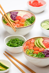 Hawaii salmon poke, avocado, rice, seaweed, cucumber, radish, carrot in bowl. Home made vegetarian poke. Seafood concept. Asian salmon poke salad on white background.