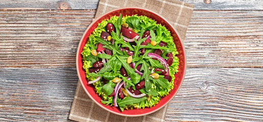 Vegan beetroot salad with red bean, lettuce, arugula, sunflower, sesame seed. Home made vegetarian beet mix leaves salad on wood background. Tasty beetroot diet dish. Top view.