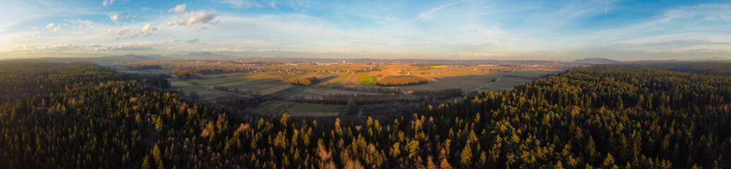 Panorama aerial view from above a forest at rural area with fields and few houses.