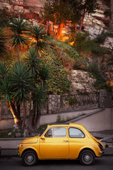 Yellow little retro car on a background of green palm trees in Italy, Sorrento. Concept: a trip on...