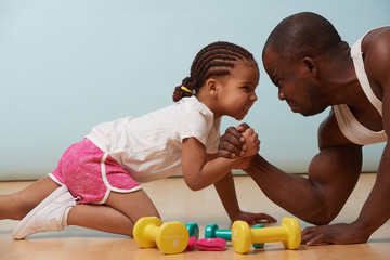 Handsome black young father is arm wrestling with his cute little daughter on the floor at home....