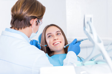 Smiling young woman is sitting in dental blue chair in clinic, office. Man doctor, orthodontist is...