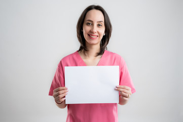 Fototapeta premium Young woman medical professional nurse or doctor dressed with pink hospital clothes holding a white paper
