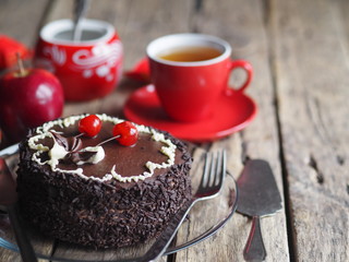 Chocolate cake with cherries on a wooden background with red apples and a Cup of tea.Close-up.