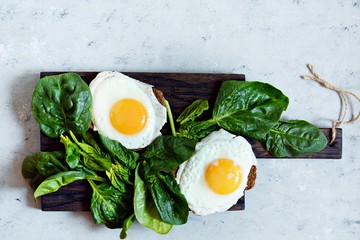 Fried eggs for breakfast with fresh spinach on rye bread toast. Hearty tasty breakfast on a blackboard on a blue background.