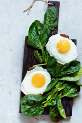Fried eggs for breakfast with fresh spinach on rye bread toast. Hearty tasty breakfast on a blackboard on a blue background.